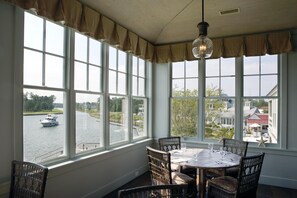 Enjoy a serene view of the water from this cozy room, featuring a round table and four chairs, a hanging light fixture, and a bay window.