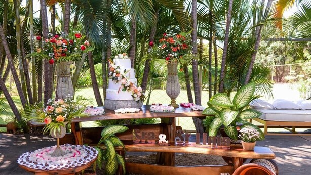 A wooden table with a tiered cake, surrounded by potted plants and a decorative sign. - Chácara Inribas accommodation and events - Goiânia - GO. (Goiânia)