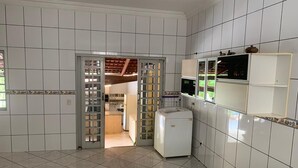 A kitchen with white tiled walls and floor, a refrigerator, and a microwave. - Chácara Inribas accommodation and events - Goiânia - GO. (Goiânia)