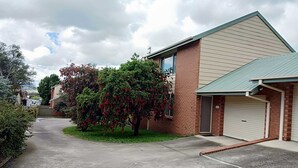 A residential property with a garage, a driveway, and a tree with red flowers. - The Bottlebrush, 2 bedroom, Villa Unit, Townhouse (Tumut)