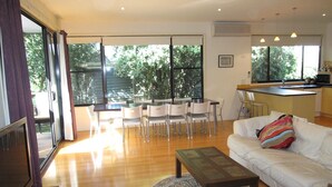Un salon moderne avec un canapé, une table basse et un coin repas comprenant des chaises et une table. On peut apercevoir la cuisine à travers une porte ouverte.