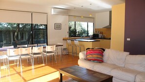 Un salon moderne avec un canapé, une table basse et un coin repas comprenant des chaises, et une cuisine en arrière-plan.