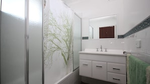 A bathroom with a glass shower enclosure, a white sink with two faucets, and a mirror above the sink.