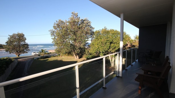 A balcony with a view of the ocean, trees, and a parked car.