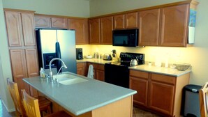 A kitchen with wooden cabinets, a stainless steel refrigerator, a microwave, a stove, and a sink.