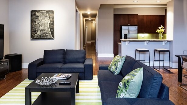 A modern living room with a sofa, coffee table, and a kitchen area with a refrigerator and bar stools. - Wrigley Field All Star Suite 3 Bedrooms 2 Bath (Chicago)