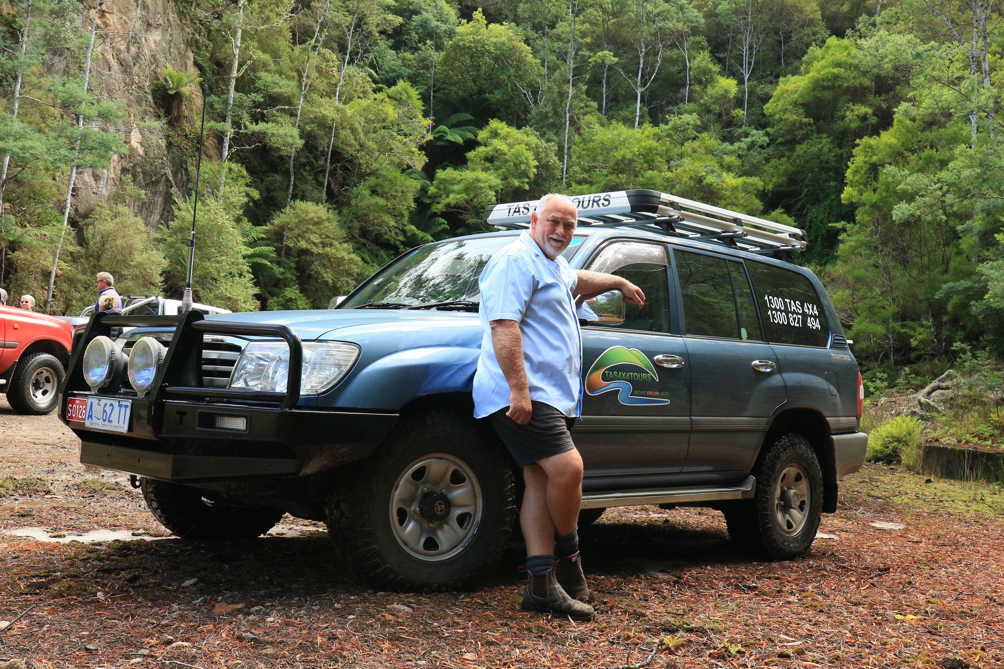 A man standing next to a vehicle with a logo and contact information on the side.