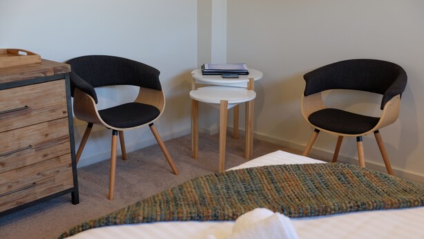 A bedroom with a bed, two chairs, a small table, and a wooden dresser. - The Tin Shed Binalong Bay, Bay of Fires, Tasmania.  (Binalong Bay)