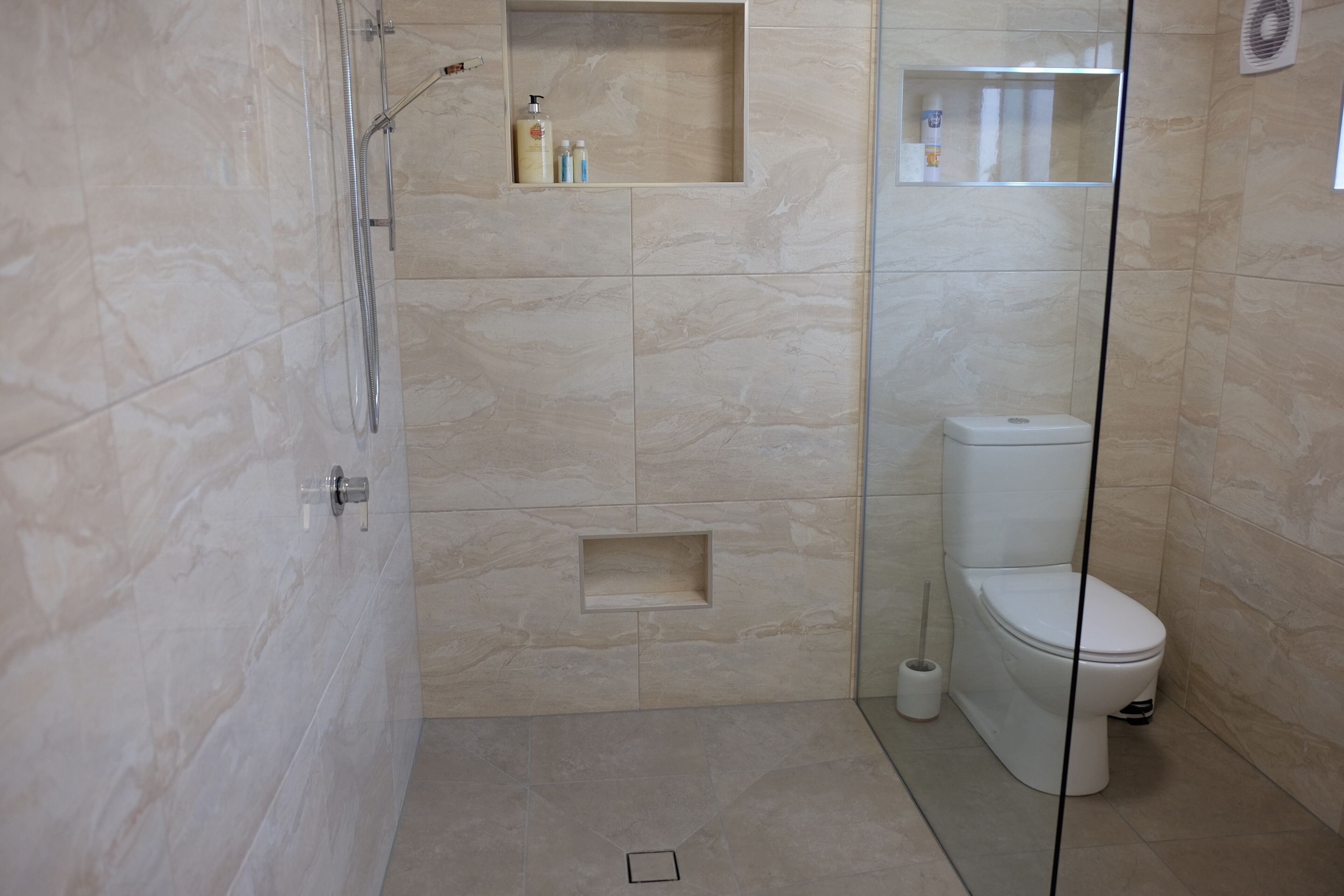 Une salle de bain moderne avec une douche à parois de verre, des toilettes et une étagère contenant des articles de toilette.