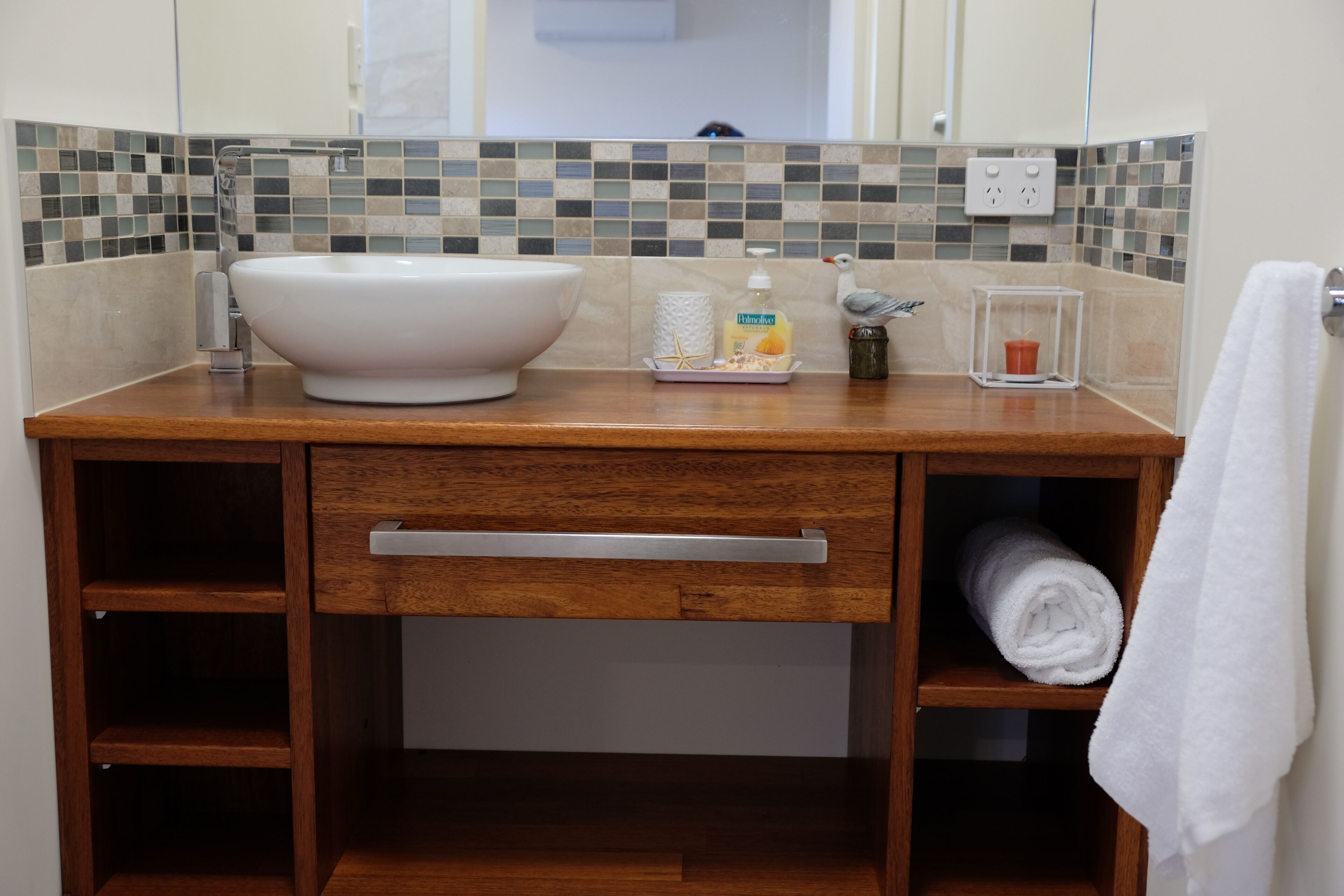 Een badkamer met een houten wastafel, een witte wasbak, een spiegel en een handdoekhouder.