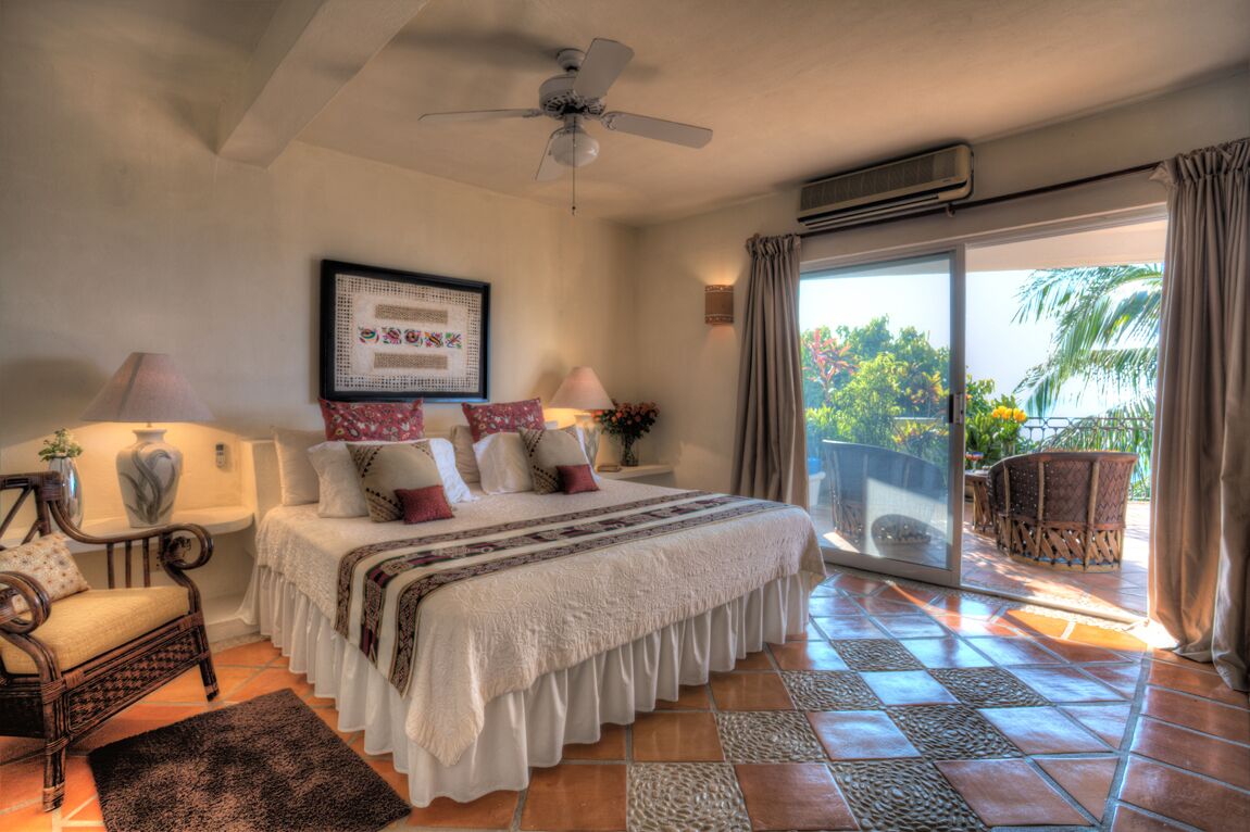 A bedroom with a bed, a chair, a ceiling fan, and a view of the outdoors through a sliding door.