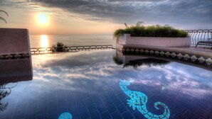 Una piscina infinita tranquila con vistas al mar, cielo iluminado por el sol y un azulejo decorativo con forma de caballito de mar.
