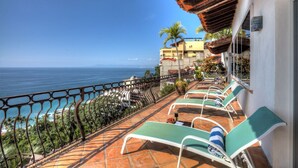Una terraza con sillones de sol con vista al océano, piso de baldosas y barandilla.