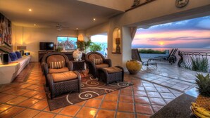 Amplia sala de estar con un sofá, dos sillones de mimbre, una mesa de centro y un televisor. El piso es de baldosas y cuenta con un ventanal con vistas panorámicas.