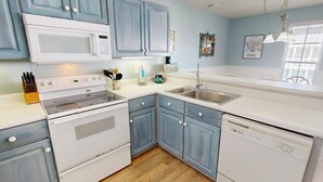A kitchen with white appliances, blue cabinets, and a wooden floor.