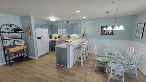 A modern kitchen with light blue cabinets, a white refrigerator, and a central island with bar stools.