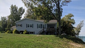A two-story house with a front porch and a small deck, surrounded by a grassy yard and trees.