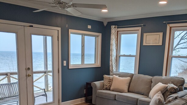 A living room with a grey sofa, a ceiling fan, and a view of the ocean through large windows.