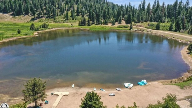 A clear lake surrounded by dense forest, a sandy beach with several boats, and a T-shaped structure on the shore. - PinecrestAreaRentals #10 Getaway Fall/labor day 3rd night free just Book 2nights (Strawberry)