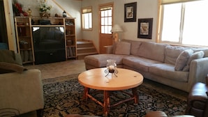 A living room with a sofa, a coffee table, a TV, a bookshelf, and a staircase. - PinecrestAreaRentals #10 Getaway Fall/labor day 3rd night free just Book 2nights (Strawberry)