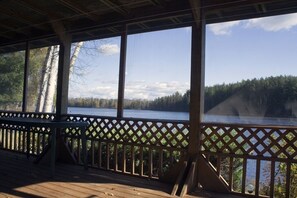 Une terrasse en bois avec une balustrade en treillis, donnant sur un lac et une forêt.
