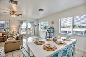 A spacious living room with a beige sofa, a dining table set with placemats, and a ceiling fan.