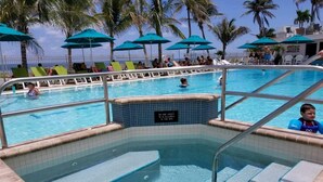 Un'area piscina con vasca idromassaggio, lettini e palme.
