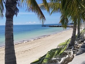 Une plage à l’eau turquoise et limpide, un rivage sablonneux et une jetée visible au loin.