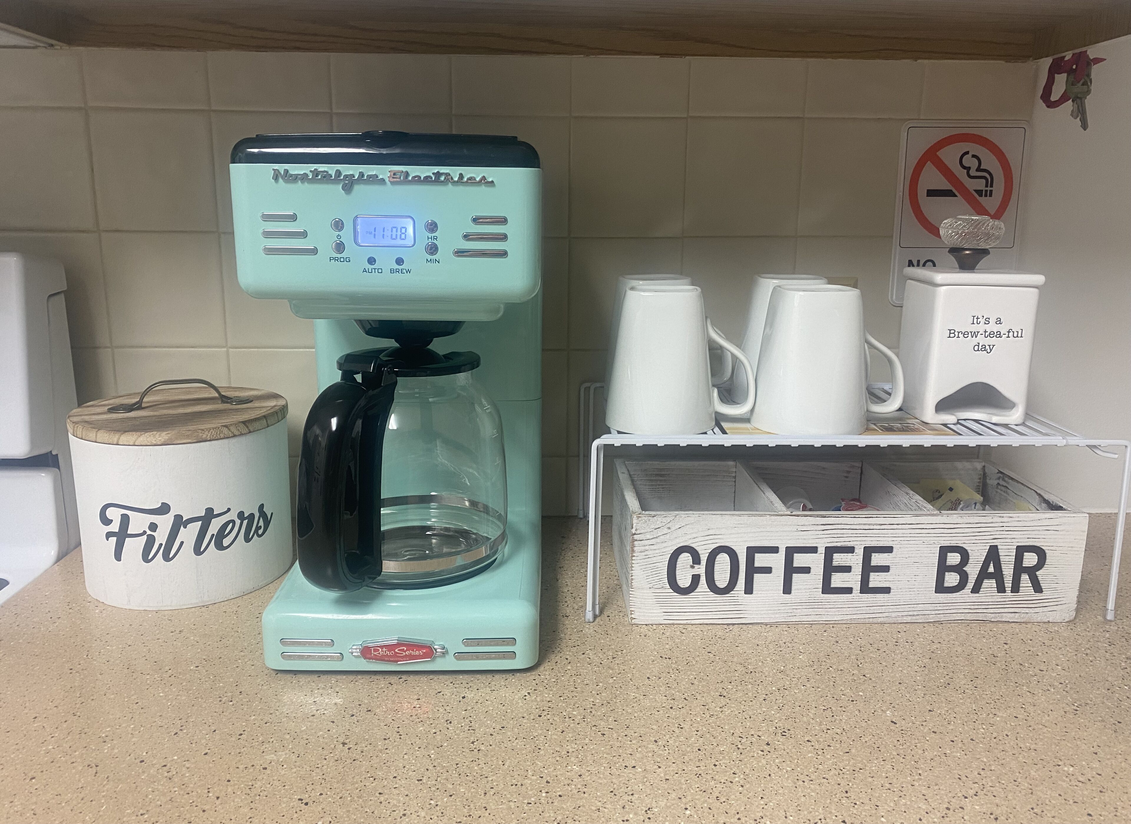A coffee maker, a container labeled 'Filters', and a 'Coffee Bar' sign on a kitchen counter.