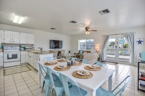 A modern kitchen with white cabinets, a dining area with blue chairs, and a ceiling fan.