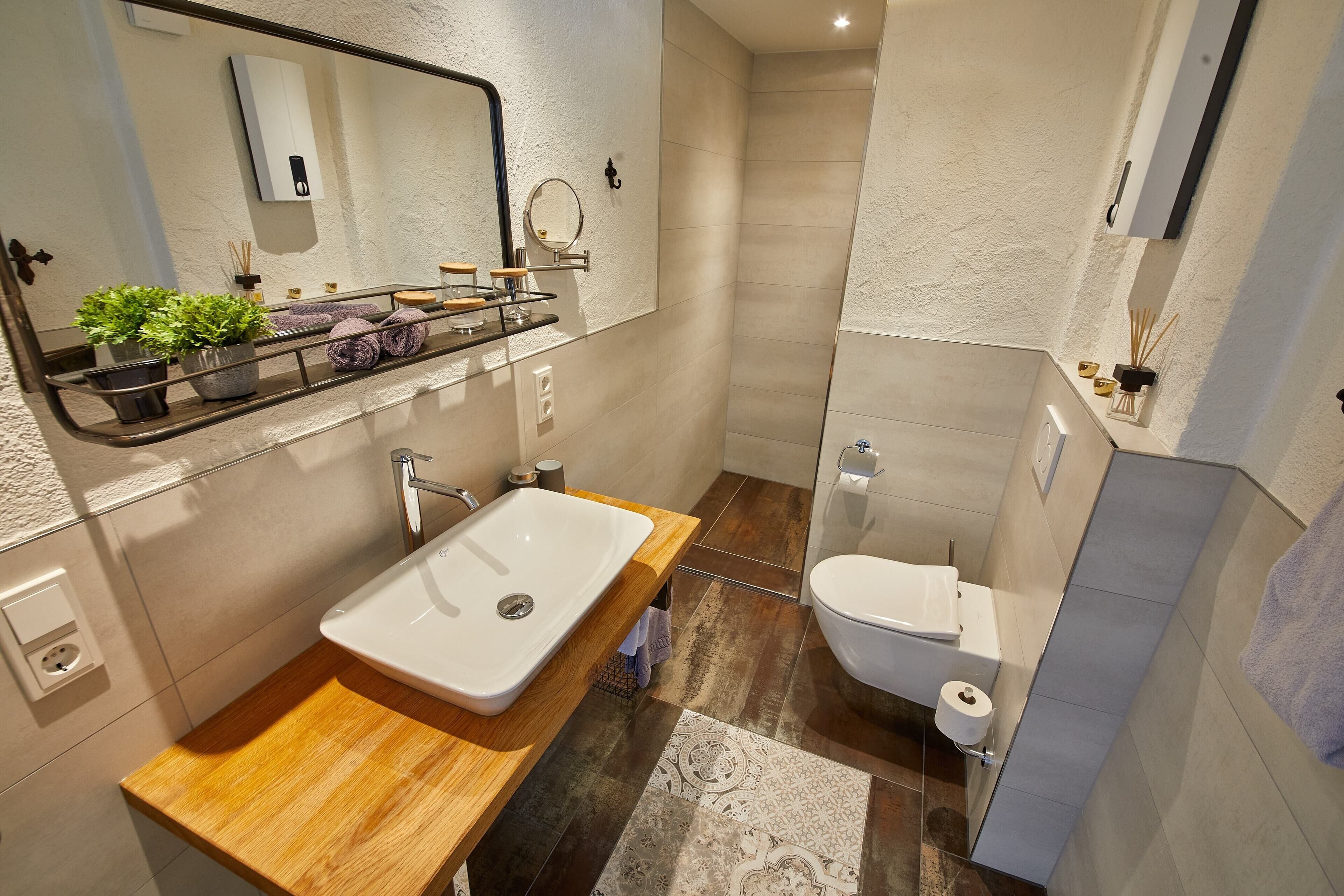 Ein modernes Badezimmer mit einem Holzkosmetikschrank, einem großen Spiegel, einer Toilette und einer Duschkabine.