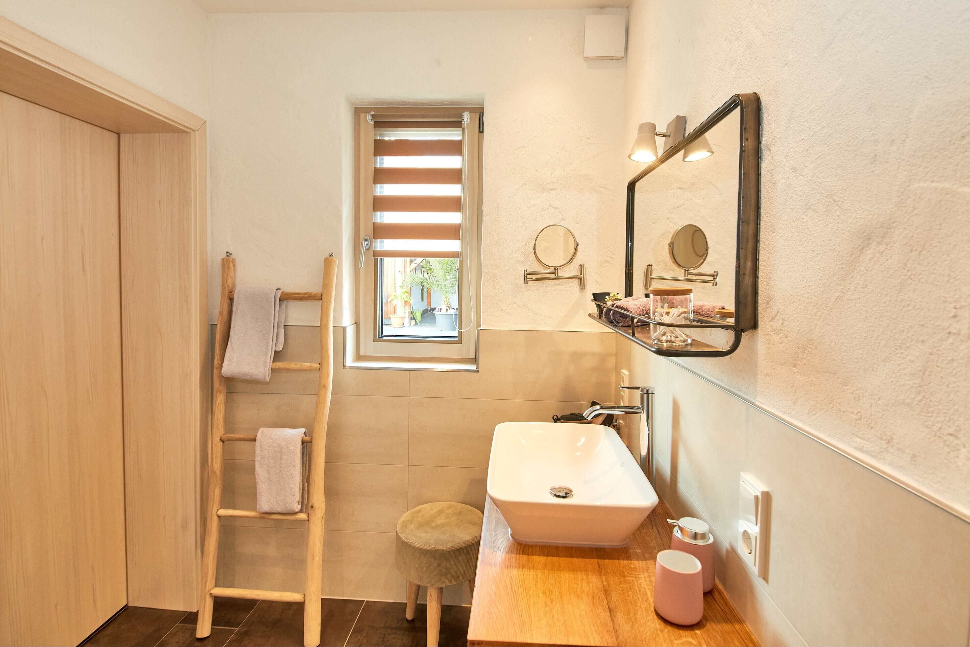 Un bagno con una scala in legno, uno sgabello, un lavandino e una finestra con persiane.