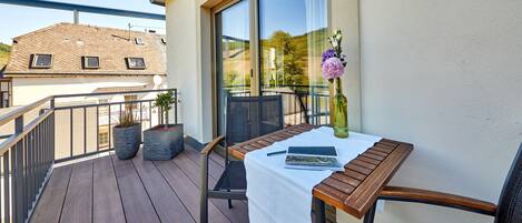 A balcony with a wooden table, two chairs, and a potted plant.