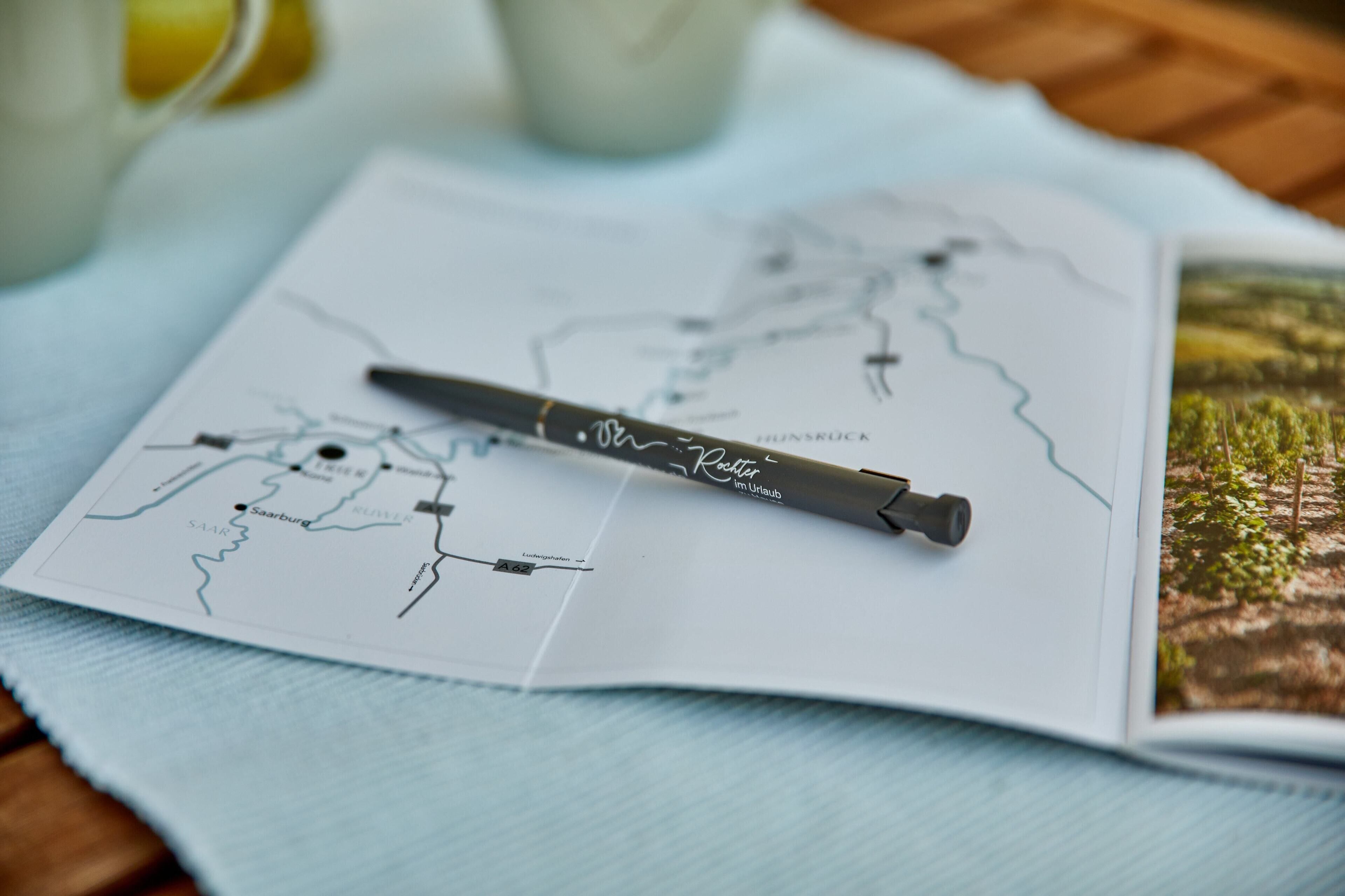 A map with a pen on top, a glass of water, and a book with a picture of a landscape.