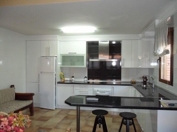 Una cocina compacta con armarios blancos, encimera negra y una isla central con taburetes.