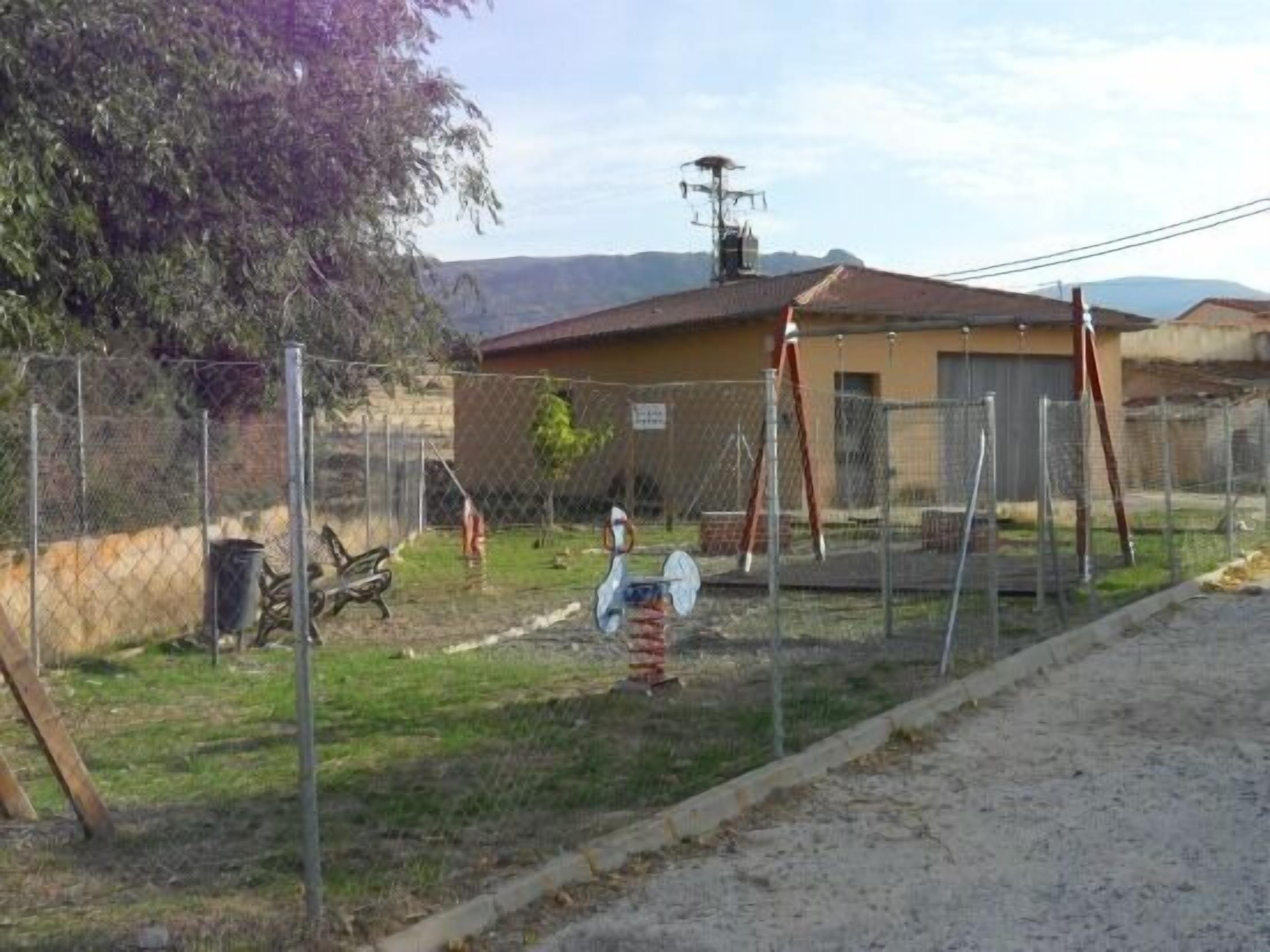 Un espace extérieur clos, avec un bâtiment en arrière-plan, un banc et une mangeoire à oiseaux.