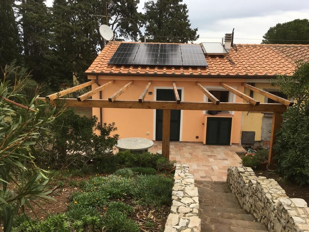 A house with a tiled roof, solar panels, a pergola, a stone pathway, and a garden.
