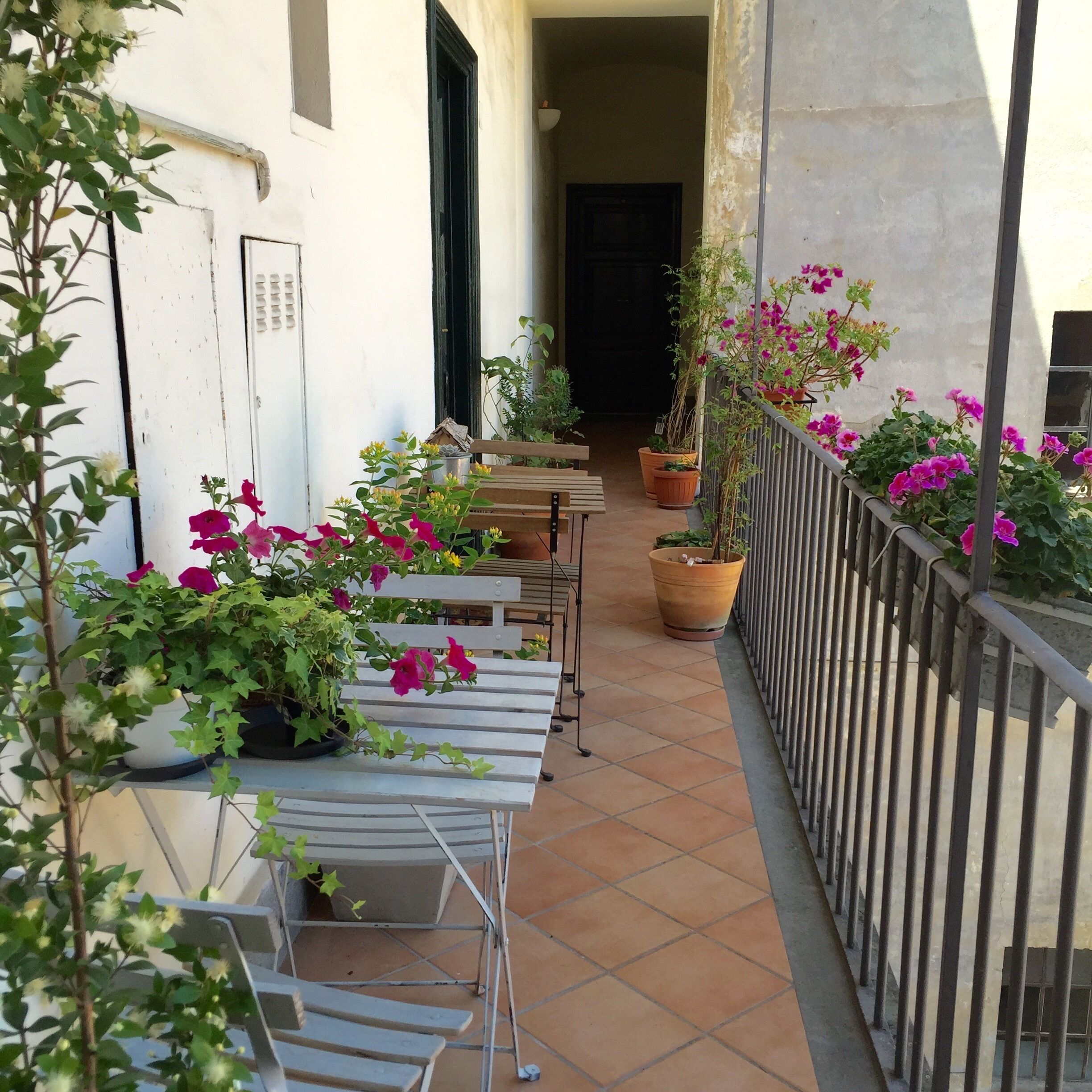 A narrow outdoor corridor with tiled flooring, potted plants, and outdoor seating.