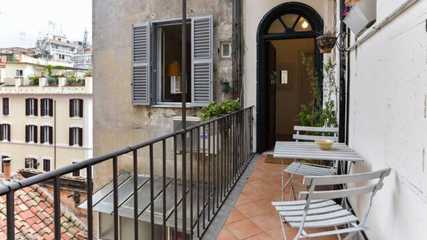 A balcony with a metal railing, a small table with a bowl, and a chair. - Rome: Delightful tiny apartment close to the Colosseum (Roma)