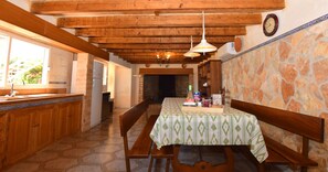 A rustic kitchen with wooden beams, a stone wall, and a dining table set with a green tablecloth. - Can Bril, Wifi free, Private pool, Garden, 15 Minutes From the beach Es Trenc (Mallorca)
