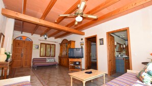 A spacious living area with a wooden ceiling, a sofa, a television on a wooden stand, and a small table. - Can Bril, Wifi free, Private pool, Garden, 15 Minutes From the beach Es Trenc (Mallorca)