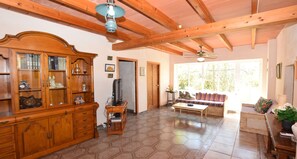 A spacious living room with wooden furniture, a television on a stand, and a ceiling fan. - Can Bril, Wifi free, Private pool, Garden, 15 Minutes From the beach Es Trenc (Mallorca)