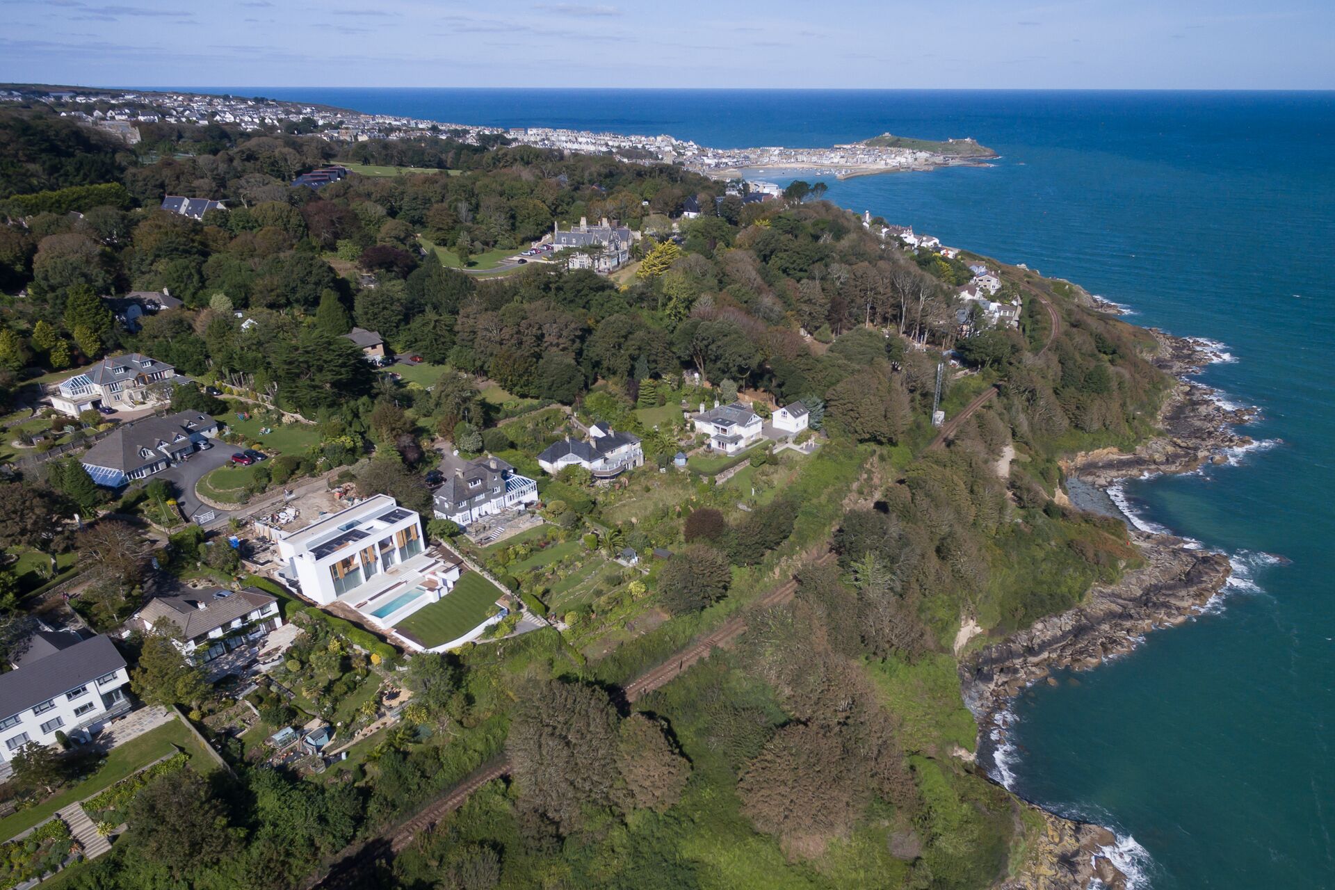An aerial view of a coastal residential area with houses, a large estate, and a coastline.