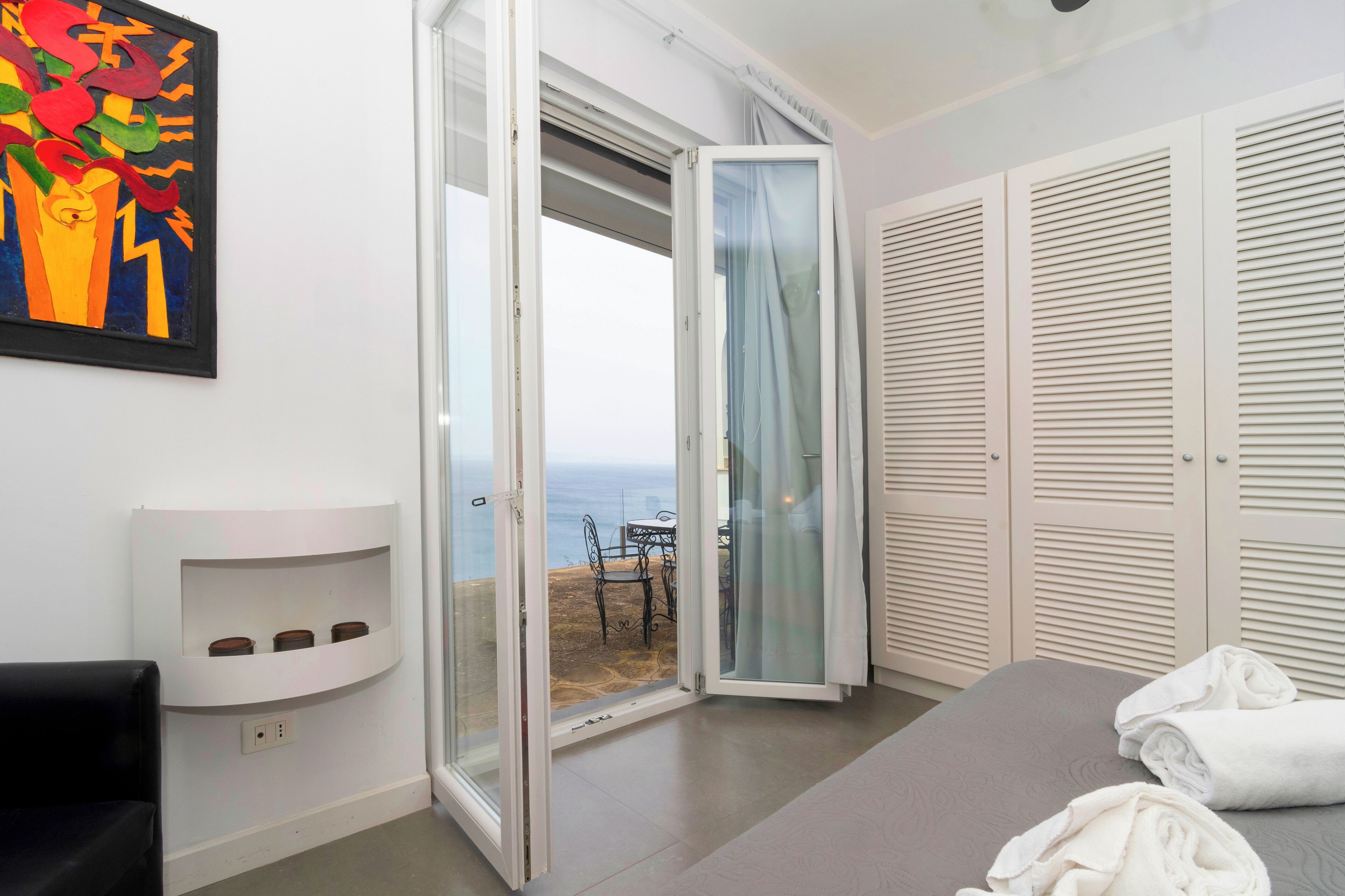 Ein Hotelzimmer mit Schiebeglastür zu einem Balkon, einem Bett, einem weißen Nachttisch und einem Bild an der Wand.