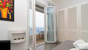 A hotel room with a sliding glass door to a balcony, a bed, a white bedside table, and a painting on the wall. - Overview exclusive seaside villa in Sorrento Peninsula (Massa Lubrense Sorrento)