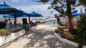 Een jachthaven met boten, blauwe parasols en buitenzitplaatsen.