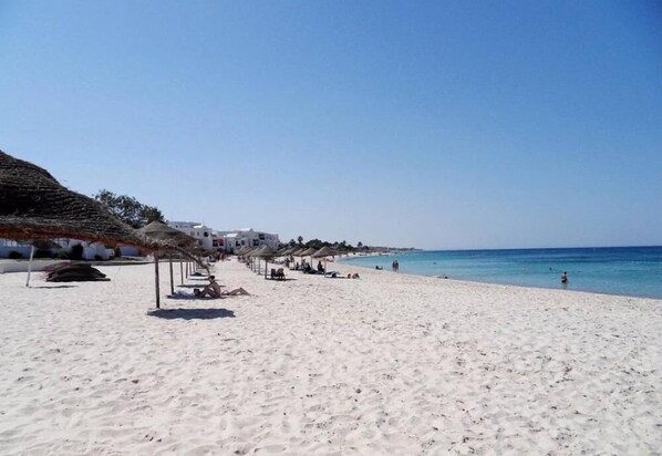Guests can relax in shaded areas beneath thatched-roof structures along the public beach.