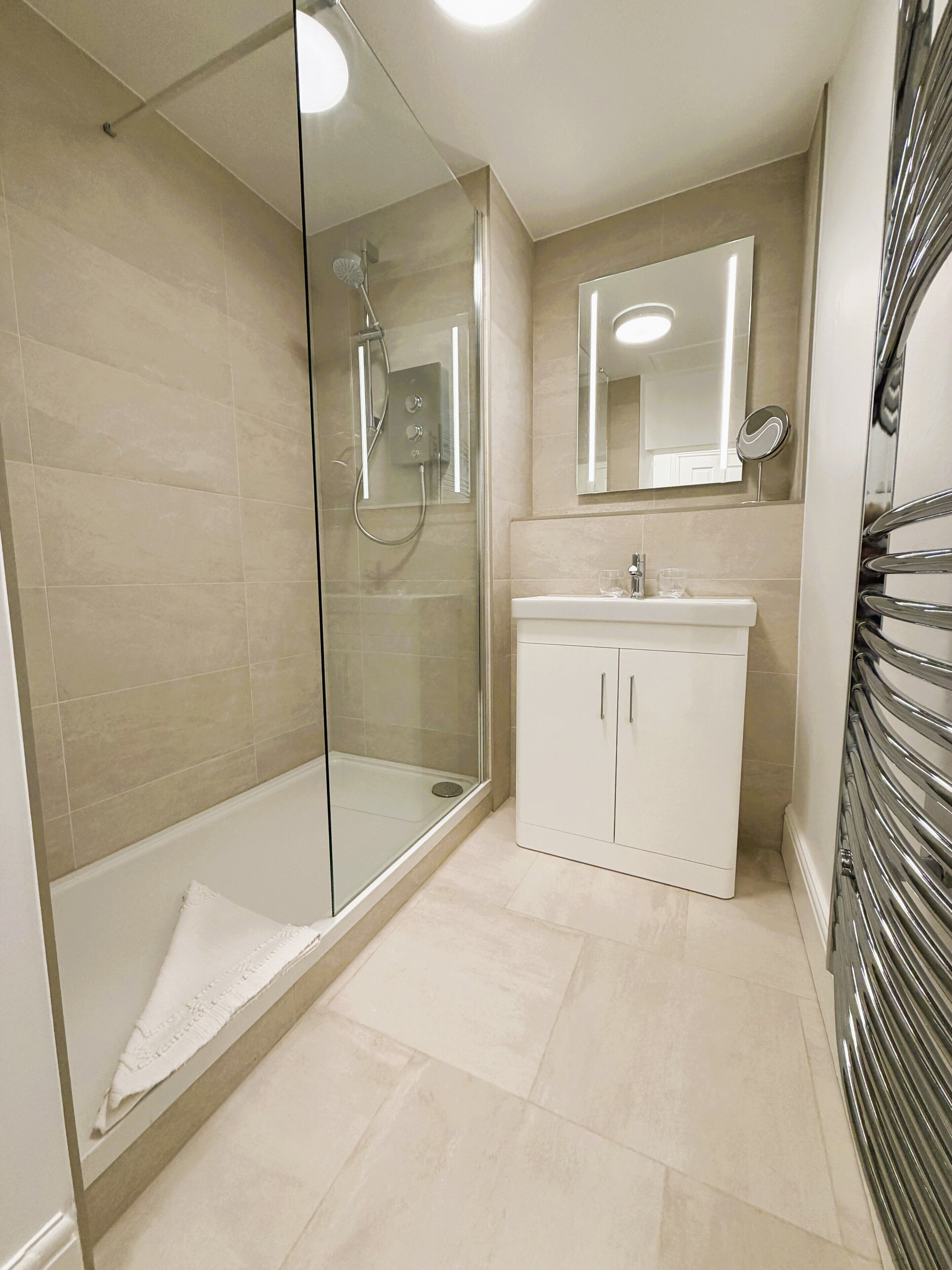 A modern bathroom with a glass-enclosed shower, a white sink with a mirror above, and a chrome towel rack.