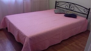 Uma cama de solteiro com colcha rosa, cabeceira de metal preto e duas almofadas.