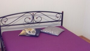 Uma cama de solteiro com colchão roxo e cabeceira de metal.